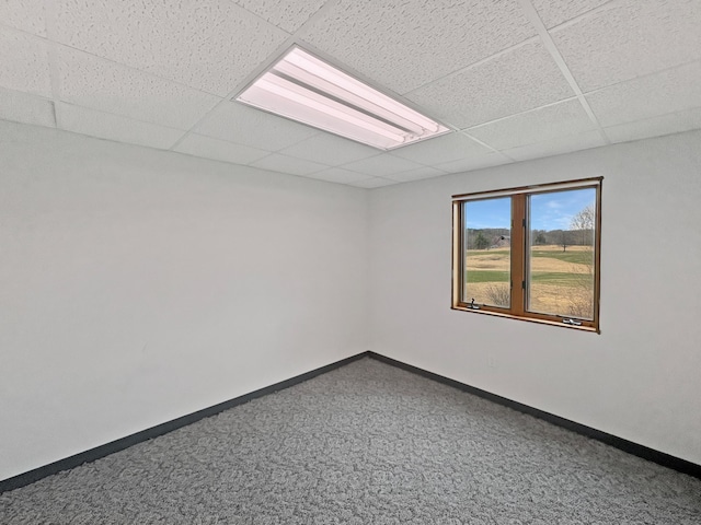 carpeted spare room featuring baseboards and a drop ceiling