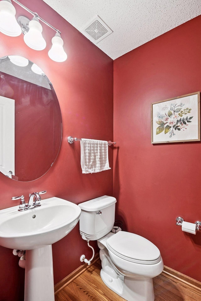 half bathroom featuring toilet, wood finished floors, baseboards, and a textured ceiling
