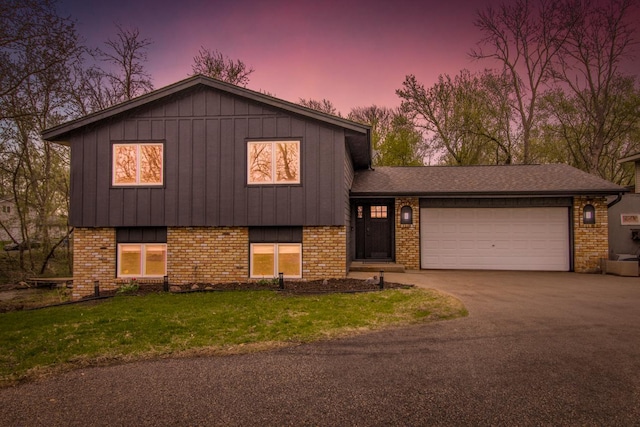 split level home featuring board and batten siding, driveway, a garage, brick siding, and a front lawn
