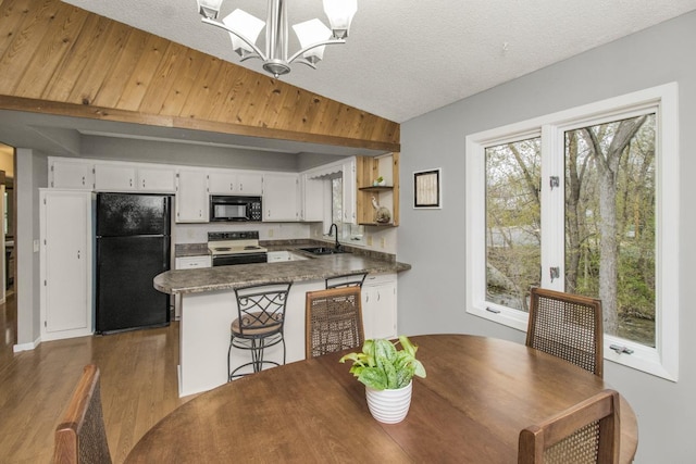 kitchen with wood finished floors, a sink, black appliances, a peninsula, and a notable chandelier