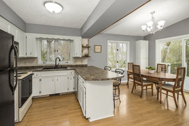 kitchen with electric range, a peninsula, dark countertops, light wood-type flooring, and a sink