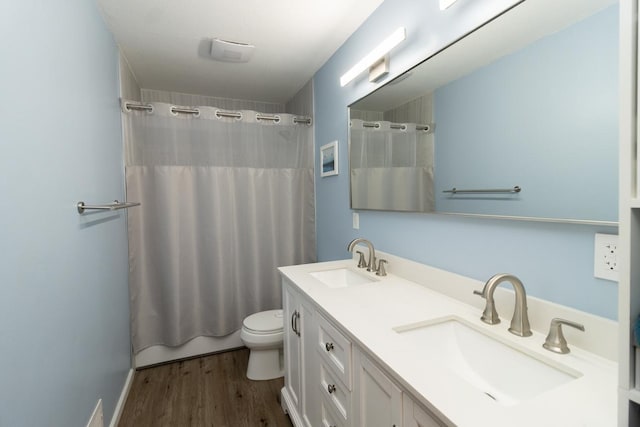 full bathroom with a sink, toilet, double vanity, and wood finished floors