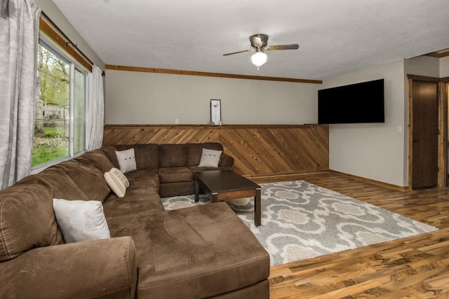 living area with baseboards, a ceiling fan, wood finished floors, and ornamental molding