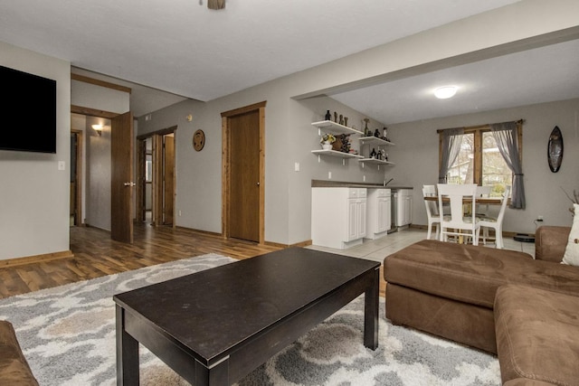 living room with baseboards, bar area, and light wood-type flooring
