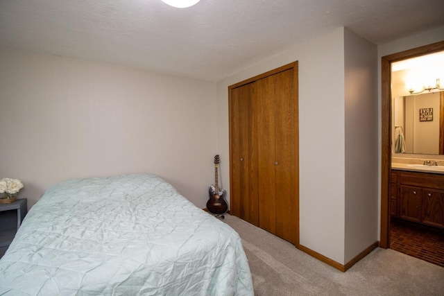 bedroom featuring light colored carpet, a sink, baseboards, a closet, and connected bathroom