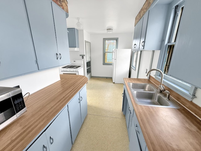 kitchen featuring white appliances, wood counters, a sink, and blue cabinets