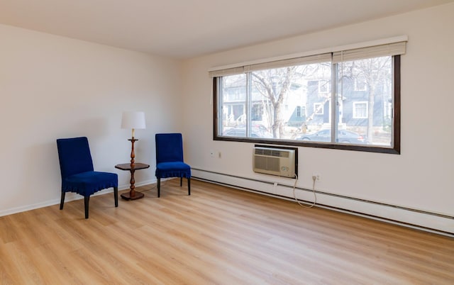 sitting room with baseboards, light wood-type flooring, a wall mounted AC, and a baseboard heating unit