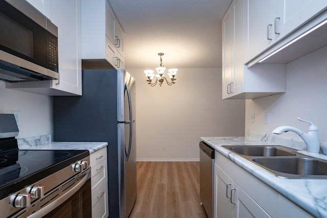 kitchen featuring white cabinets, a notable chandelier, a sink, appliances with stainless steel finishes, and light wood-style flooring