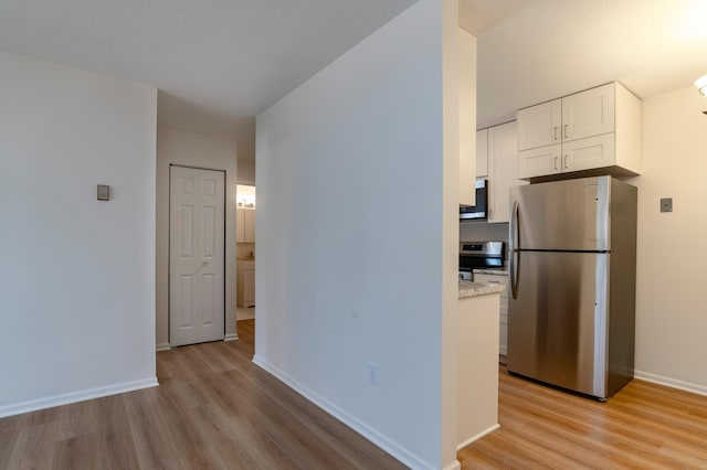 kitchen with white cabinetry, light wood-style flooring, appliances with stainless steel finishes, and baseboards