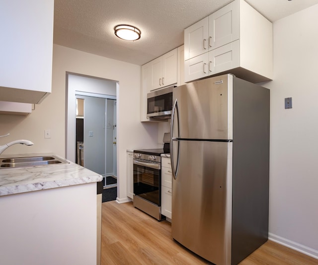 kitchen featuring a sink, appliances with stainless steel finishes, a textured ceiling, white cabinetry, and light wood finished floors