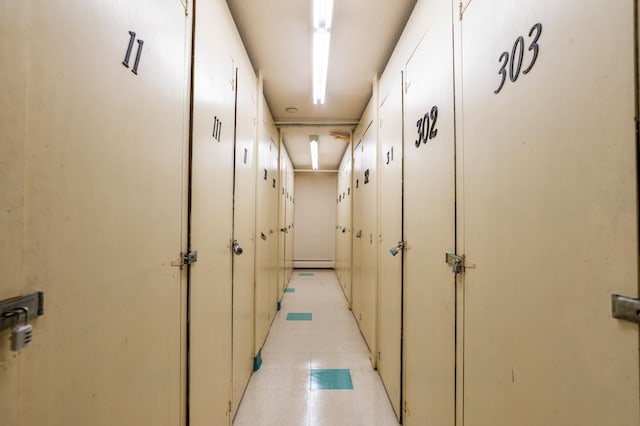 corridor with a baseboard heating unit and light tile patterned floors