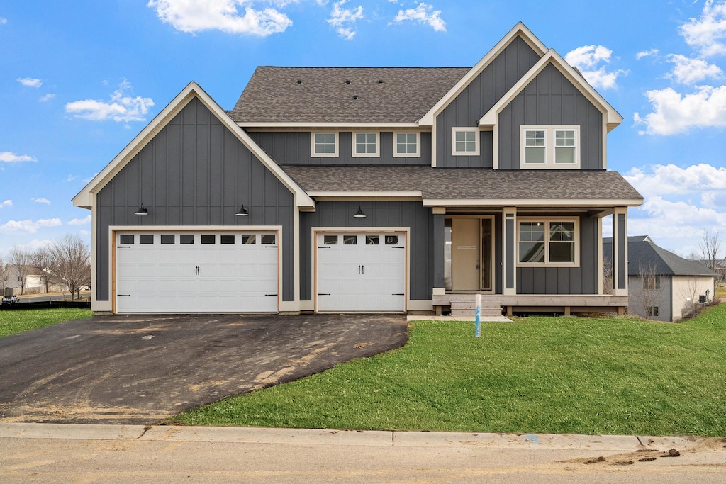 view of front of house featuring board and batten siding, a shingled roof, aphalt driveway, and a front yard
