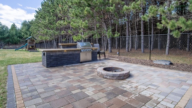 view of patio featuring a fire pit, a fenced backyard, grilling area, a playground, and an outdoor kitchen
