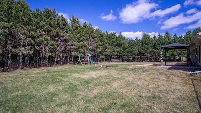 view of yard featuring a forest view, fence, a playground, and a gazebo