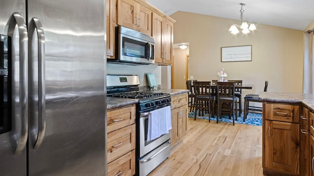 kitchen featuring hanging light fixtures, a notable chandelier, stainless steel appliances, light wood-style flooring, and lofted ceiling