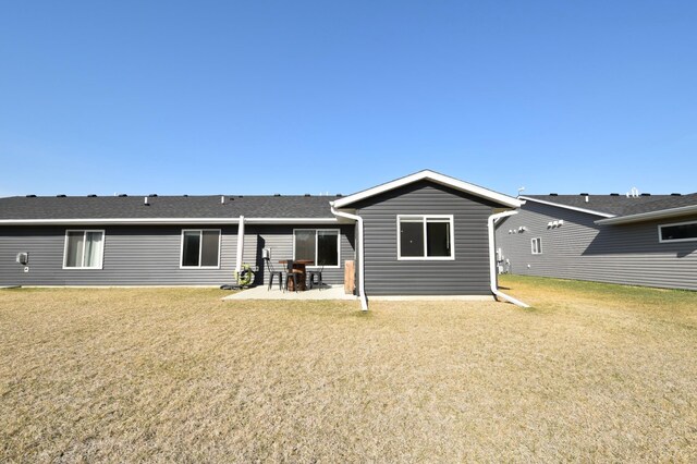 rear view of house with a patio, roof with shingles, and a lawn