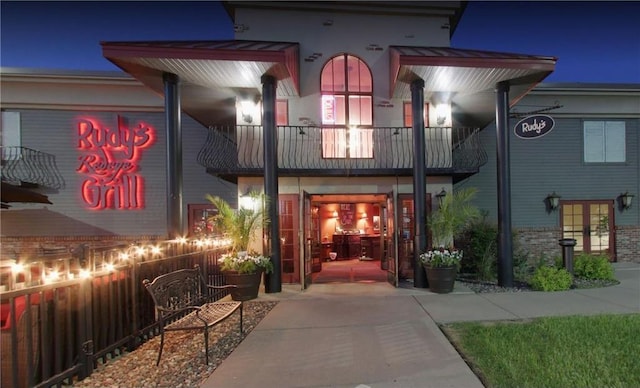 exterior entry at twilight with a balcony, fence, and brick siding