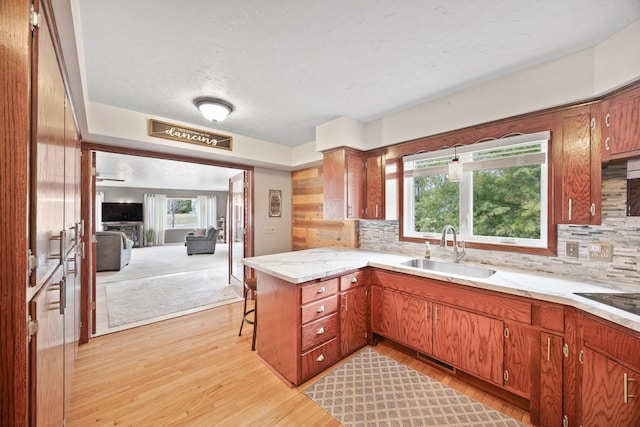 kitchen with decorative backsplash, a breakfast bar area, a sink, light wood finished floors, and a peninsula