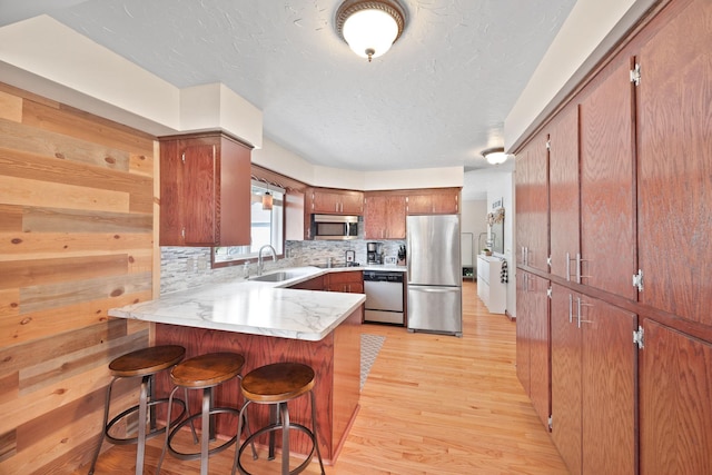 kitchen with appliances with stainless steel finishes, tasteful backsplash, a sink, a peninsula, and light wood-style flooring