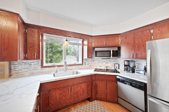 kitchen with brown cabinets, light stone counters, a sink, appliances with stainless steel finishes, and backsplash