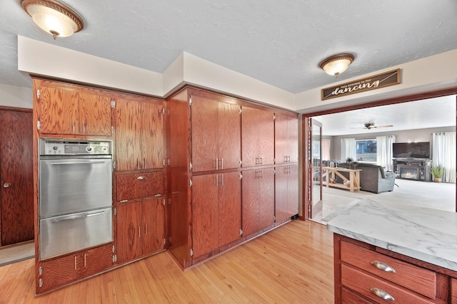 kitchen featuring light wood-style floors, stainless steel oven, light countertops, a ceiling fan, and a warming drawer