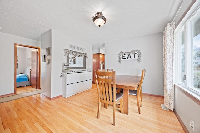 dining room featuring a textured ceiling, baseboards, visible vents, and light wood-type flooring
