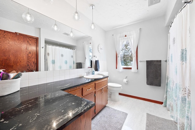 bathroom with vanity, toilet, a textured ceiling, baseboards, and visible vents