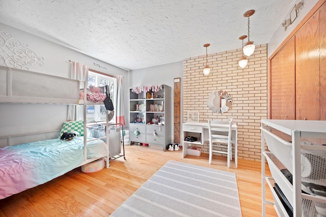 bedroom with brick wall, a textured ceiling, and light wood-style flooring