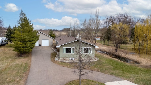 view of front of house featuring a garage, a front lawn, aphalt driveway, a chimney, and an outbuilding