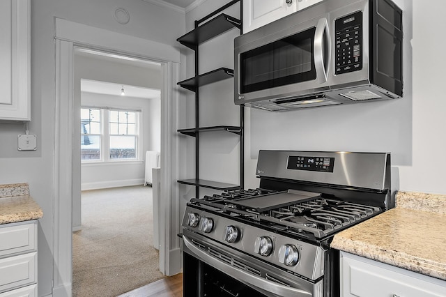 kitchen with ornamental molding, carpet floors, appliances with stainless steel finishes, and white cabinetry