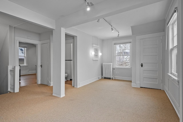 unfurnished bedroom featuring baseboards, carpet, radiator, ensuite bath, and rail lighting