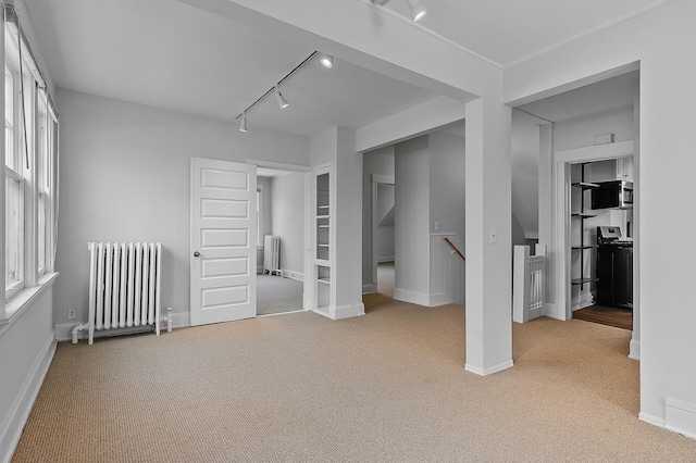 unfurnished bedroom with radiator heating unit, carpet floors, baseboards, and track lighting