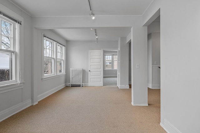 carpeted empty room with radiator heating unit, baseboards, and rail lighting