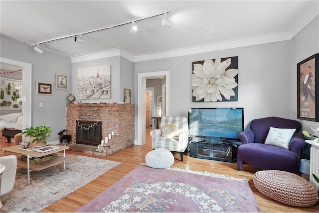 living area with wood finished floors, track lighting, a brick fireplace, and ornamental molding