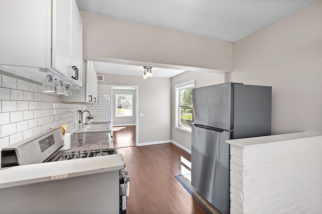 kitchen with white cabinets, a sink, dark wood finished floors, appliances with stainless steel finishes, and backsplash
