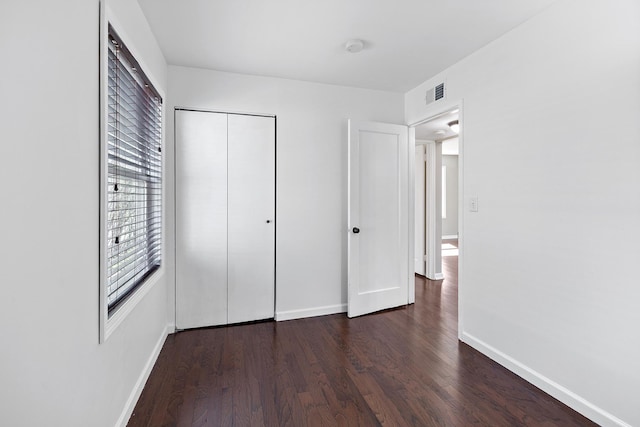 unfurnished bedroom with baseboards, a closet, wood finished floors, and visible vents