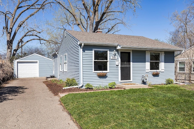 view of front of property featuring an outdoor structure, a front yard, a chimney, driveway, and a detached garage