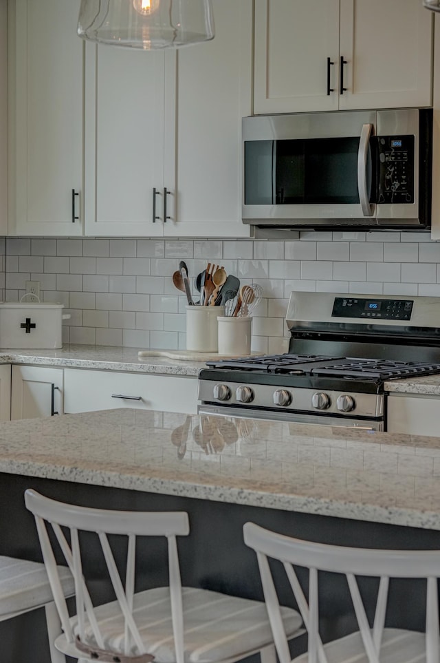 11422 34th St N, Lake Elmo, MN 55042 - kitchen featuring stainless steel appliances, light stone countertops, white cabinets, backsplash, and decorative light fixtures