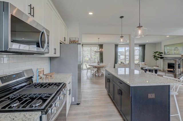 11422 34th St N, Lake Elmo, MN 55042 - kitchen featuring appliances with stainless steel finishes, open floor plan, white cabinets, backsplash, and light wood-style flooring