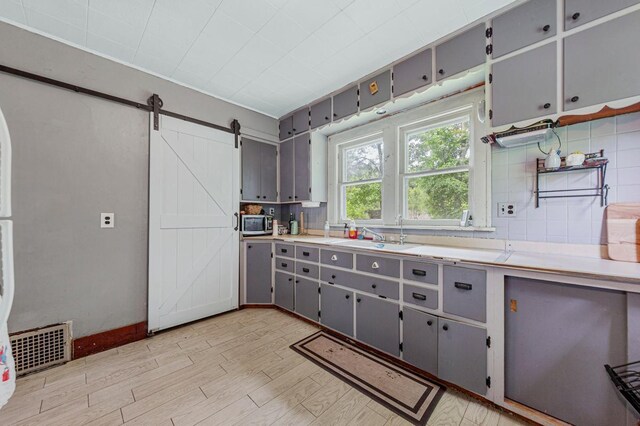 32673 Rosewood Ln, Saint Peter, MN 56082 - kitchen featuring gray cabinetry, a sink, stainless steel microwave, a barn door, and light wood-type flooring