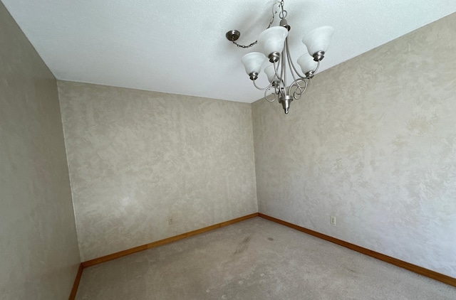 carpeted empty room with a notable chandelier and baseboards