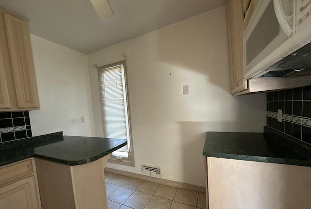kitchen featuring white microwave, visible vents, light tile patterned flooring, dark countertops, and backsplash