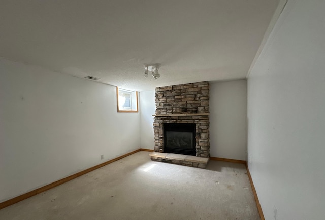 unfurnished living room with carpet flooring, visible vents, a stone fireplace, and baseboards