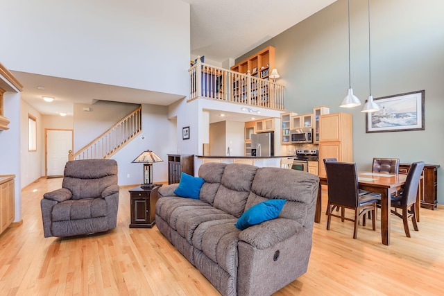 living room with light wood-type flooring, a towering ceiling, baseboards, and stairs