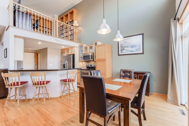 dining area featuring visible vents, baseboards, light wood-type flooring, and a high ceiling
