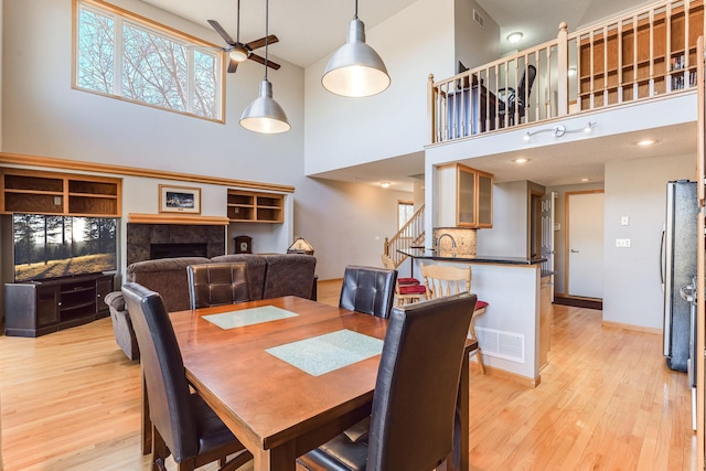 dining area with light wood-style flooring, a high ceiling, a ceiling fan, and visible vents