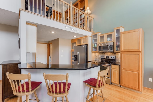 kitchen with light wood-style floors, a peninsula, stainless steel appliances, a breakfast bar area, and backsplash