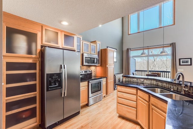 kitchen featuring backsplash, dark countertops, light wood-style floors, appliances with stainless steel finishes, and a sink