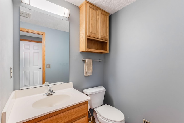 half bathroom featuring visible vents, toilet, vanity, and a textured ceiling