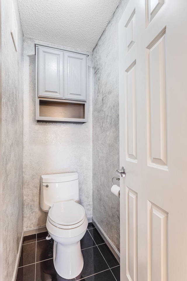 bathroom with toilet, baseboards, and tile patterned flooring
